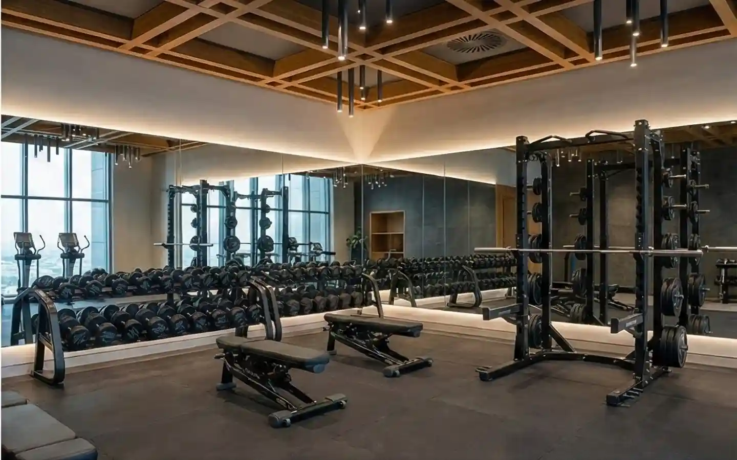 Boutique gym interior featuring a wooden coffered ceiling with pendant lighting, full-length mirrors, and professional weightlifting racks