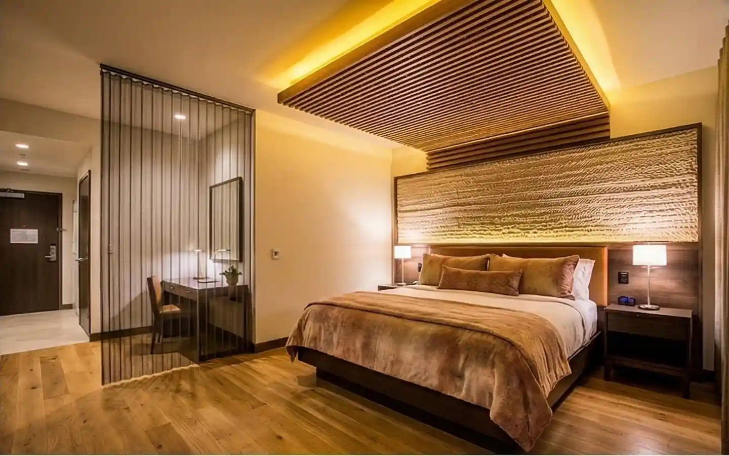 Warm boutique hotel bedroom design featuring a textured stone headboard, wood slat ceiling with cove lighting, and a private work desk separated by a metal mesh screen