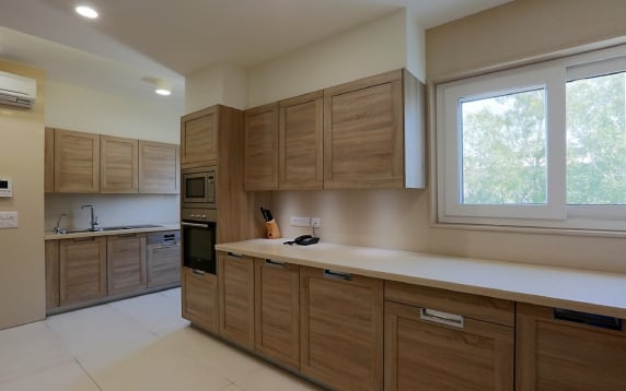 Bright, modern kitchen interior design featuring light wood cabinets, long white countertops, built-in stainless steel appliances, and a large window letting in natural light