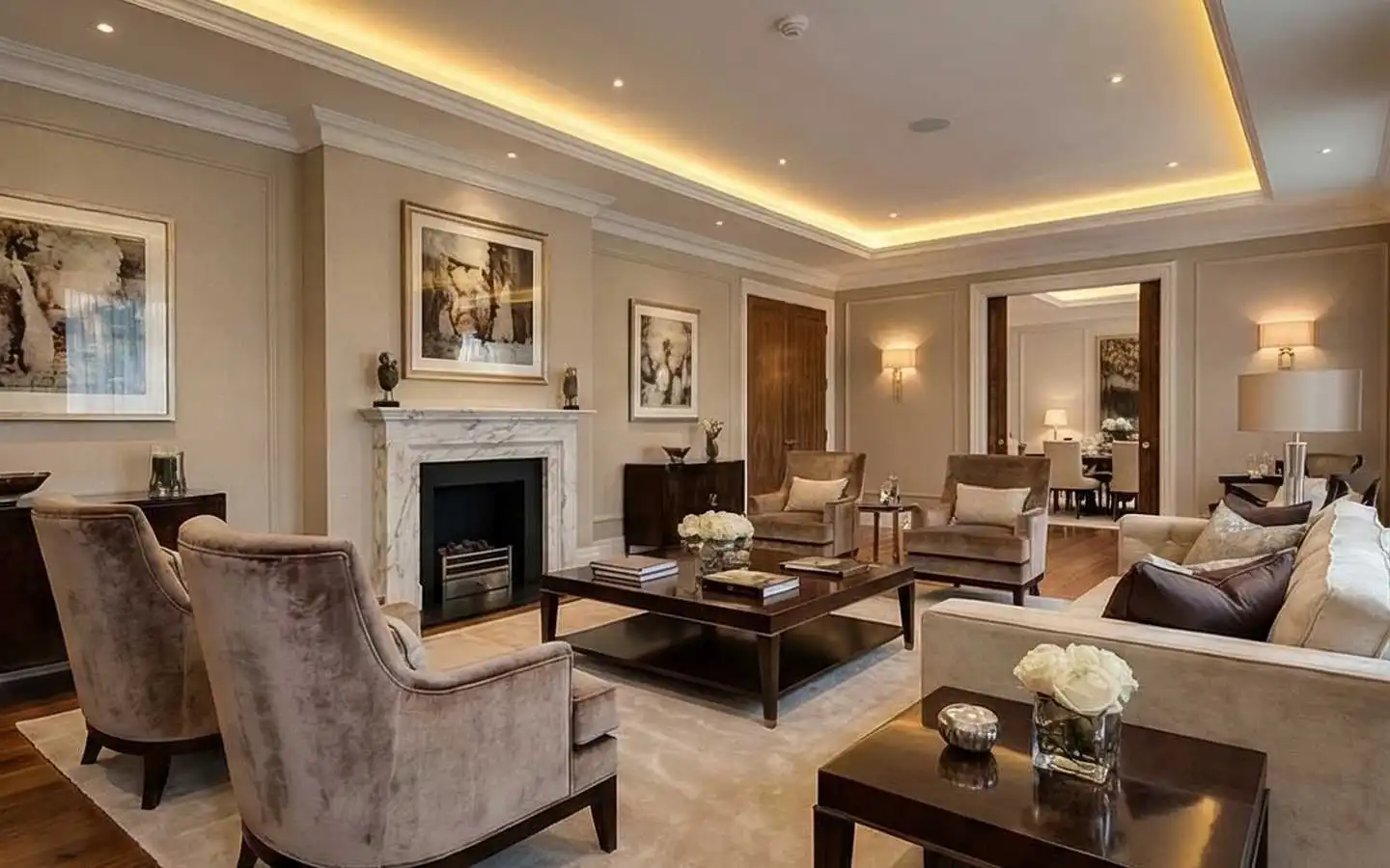 Formal luxury living room featuring a white marble fireplace, velvet armchairs, dark wood coffee table, and elegant cove lighting