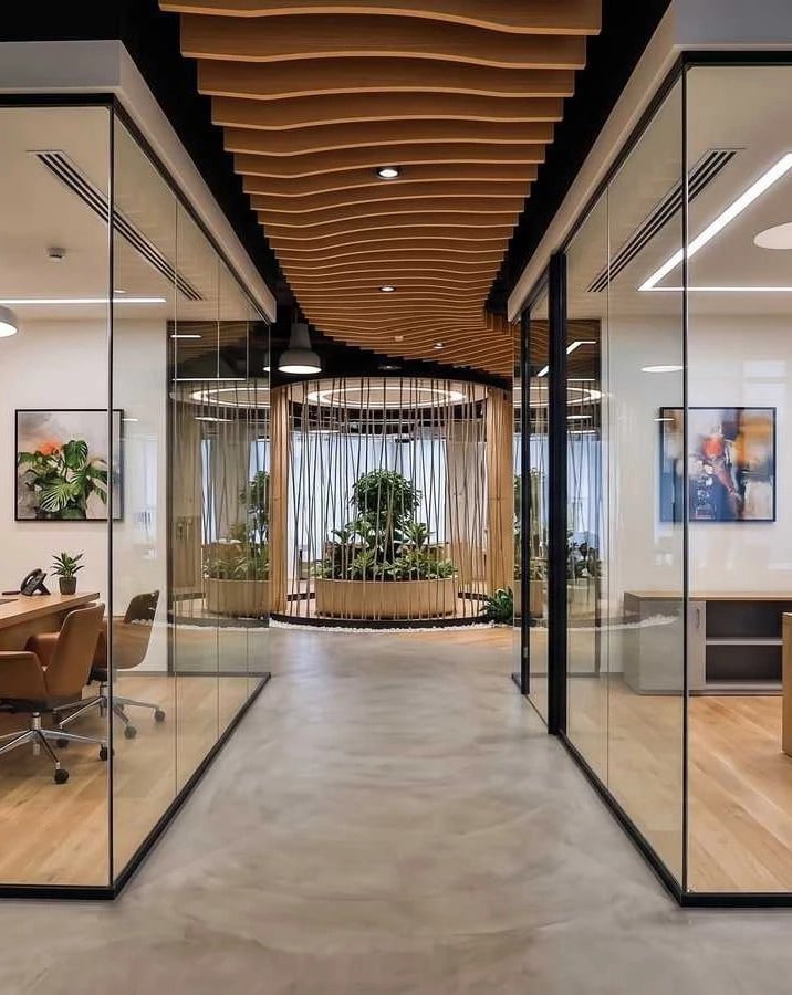 Contemporary office corridor featuring floor-to-ceiling glass partitions, a wave-patterned wooden ceiling, and a central biophilic planter feature