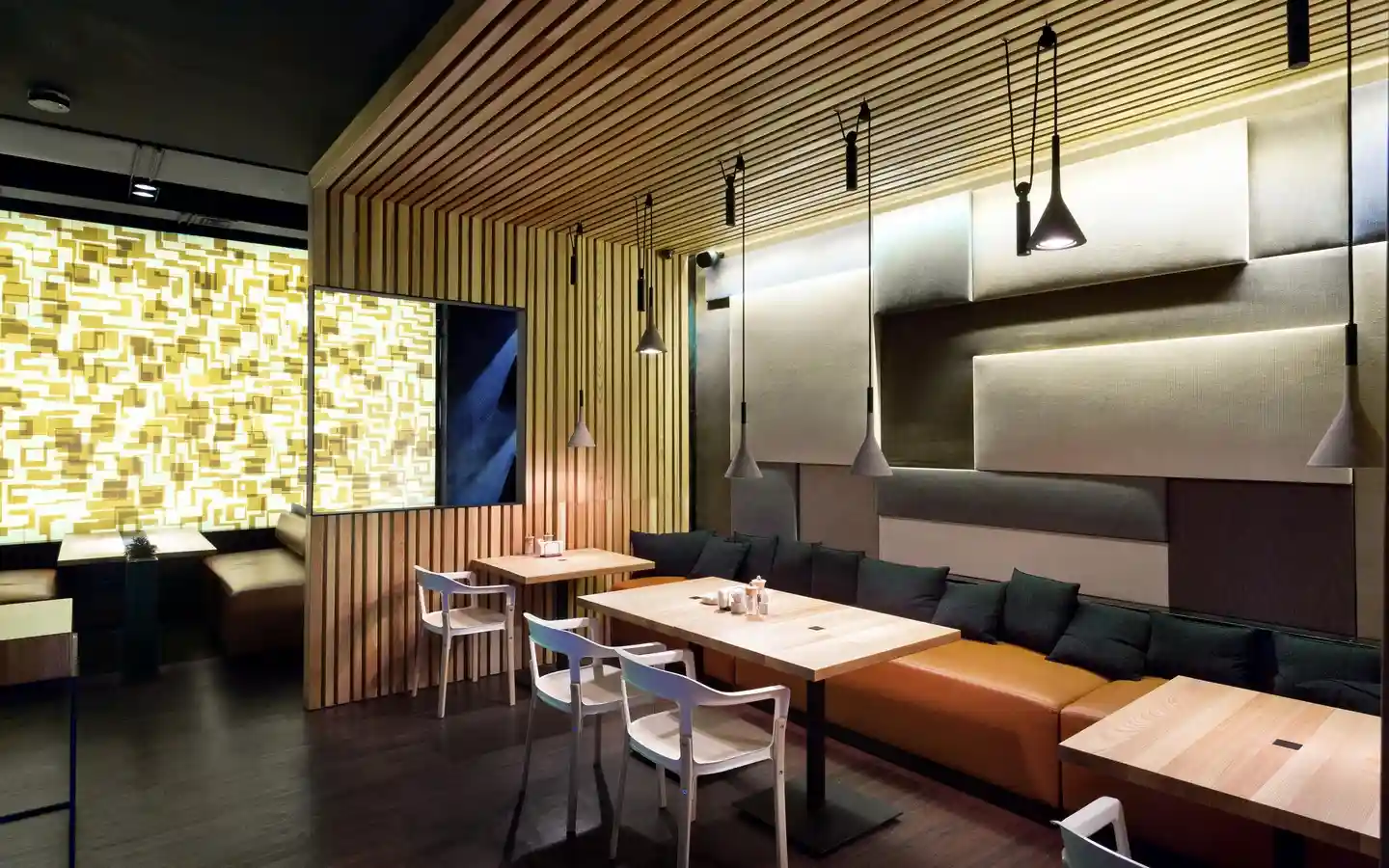 Contemporary restaurant interior featuring a timber slat ceiling and wall partition, tan leather banquette seating with black pillows, and geometric 3D wall panels with integrated backlighting