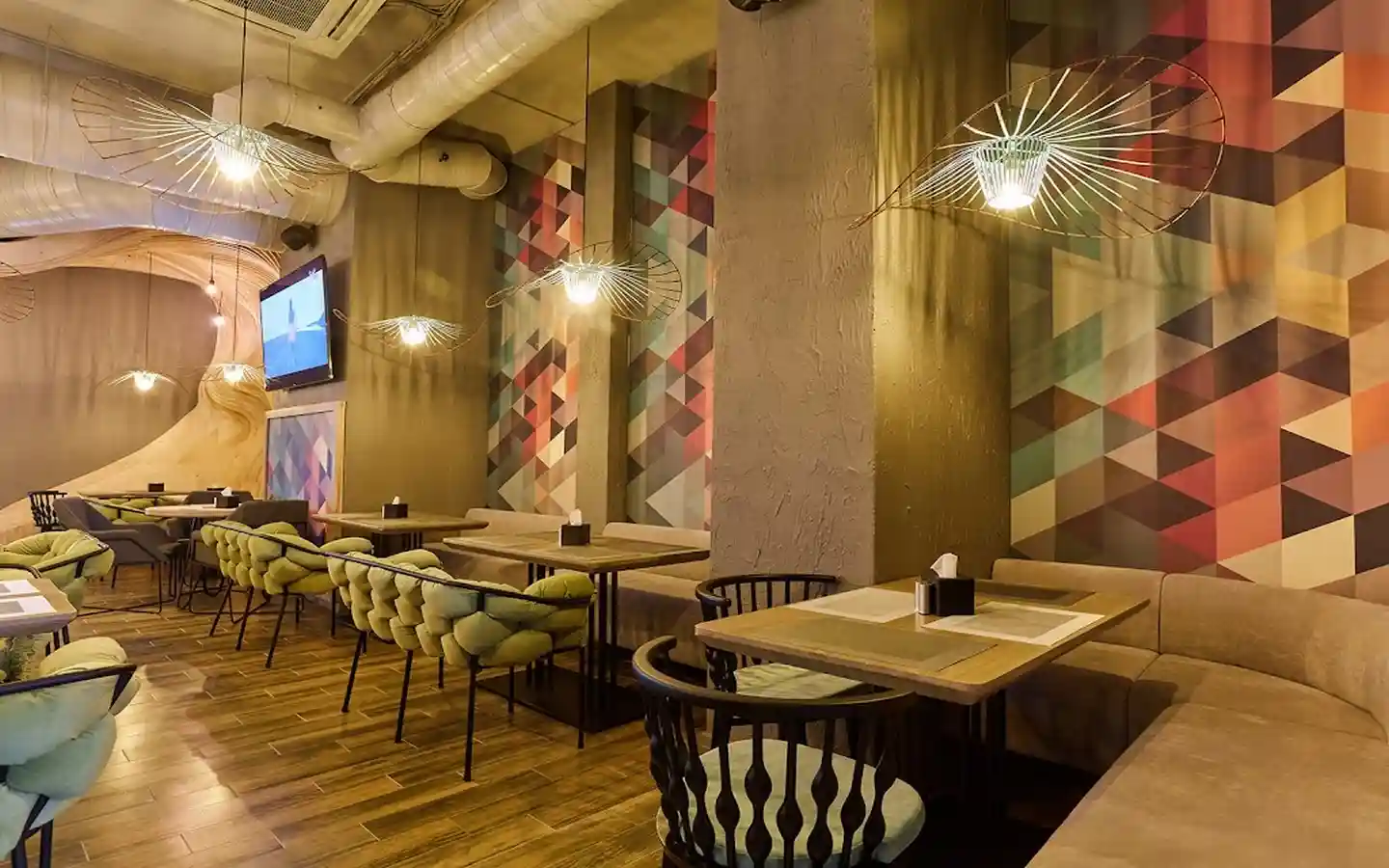 Eclectic restaurant interior featuring geometric triangle wallpaper, unique wire pendant lights, and light green tufted chairs