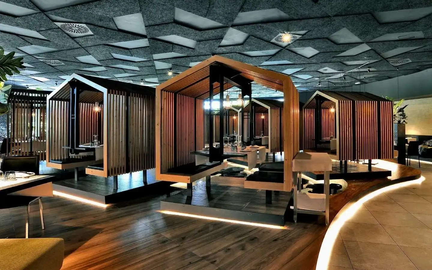 Creative restaurant interior featuring house-shaped wooden dining booths, integrated LED floor lighting, and a modern geometric acoustic tile ceiling