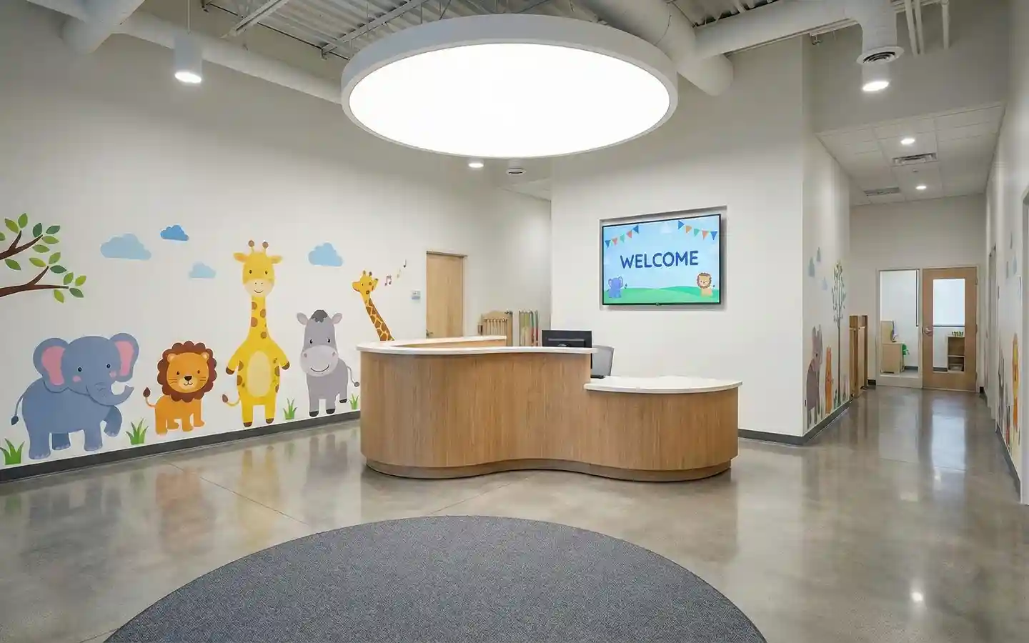 Modern daycare lobby featuring a curved wood reception desk, animal wall graphics, and a circular halo ceiling light