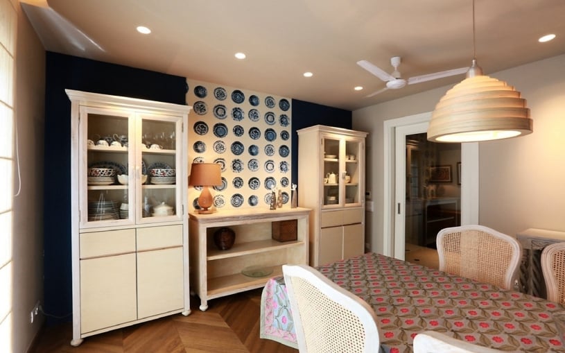 Eclectic dining room featuring a navy blue accent wall with decorative ceramic plates, white glass-front cabinets, and a chevron wood floor