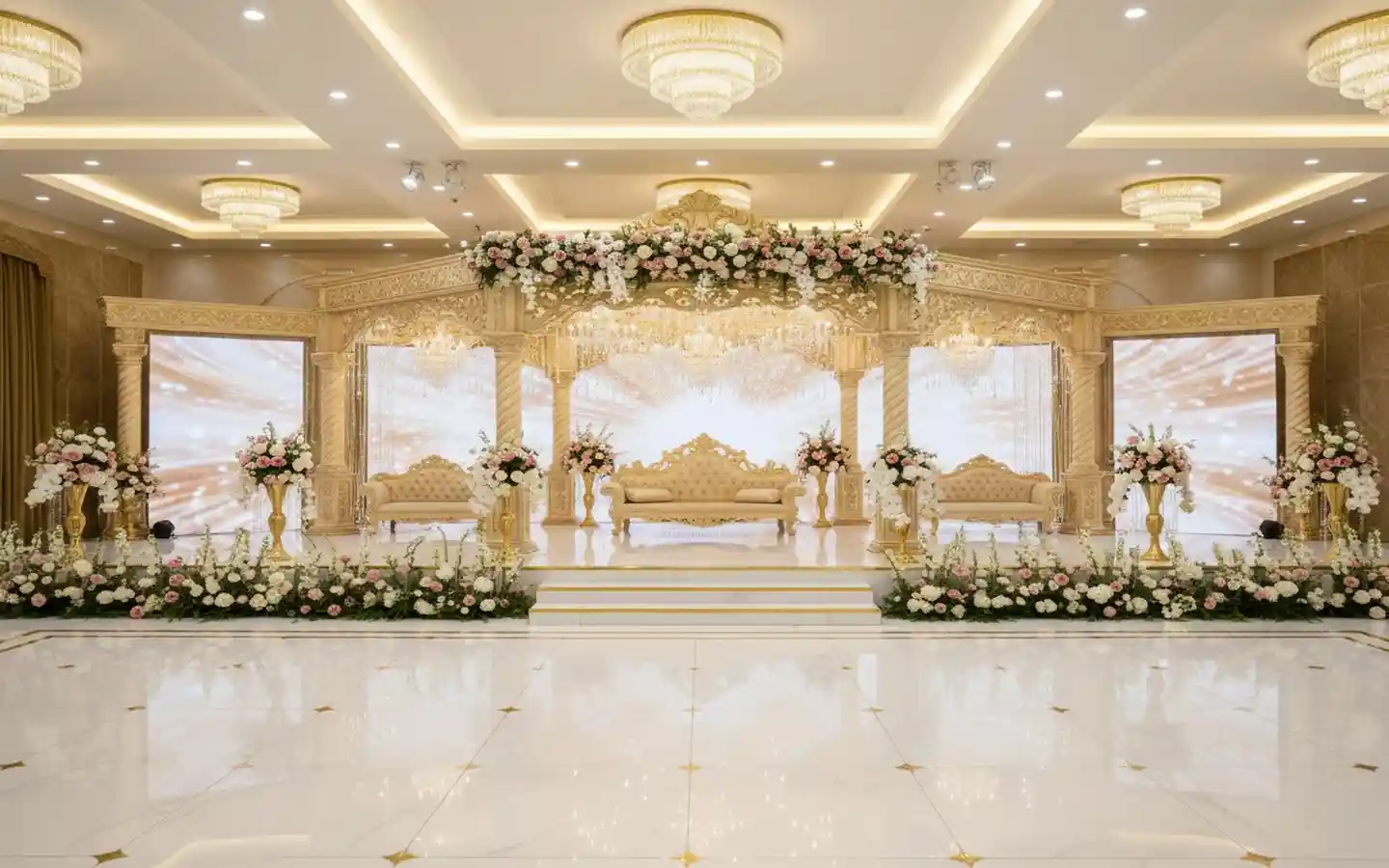 Elegant wedding stage interior decoration with a carved gold mandap, floral arrangements, luxury sofa seating, and warm ambient ceiling lighting