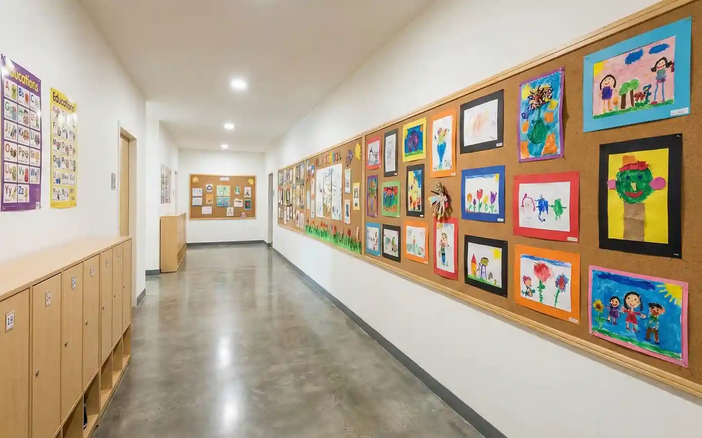 Bright elementary school hallway featuring light wood lockers, polished concrete floors, and a long corkboard wall displaying colorful student artwork