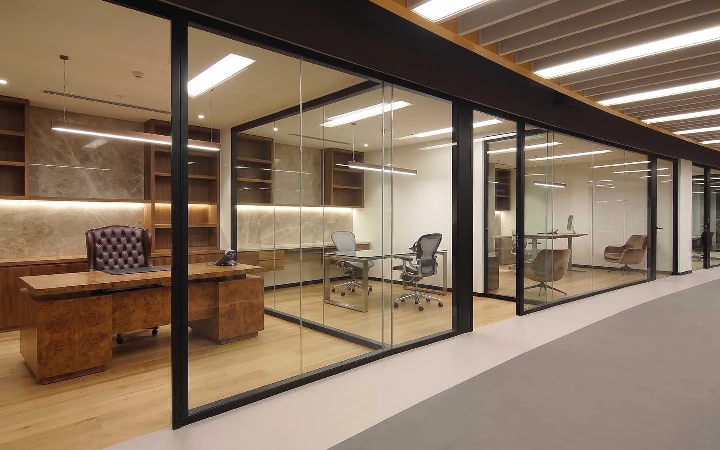 Luxury executive office interior featuring glass partitions, wood burl desks, leather captain chairs, and built-in shelving with marble backsplashes