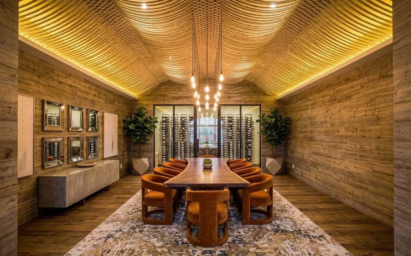 Modern industrial farmhouse dining room featuring a long live-edge wood table, orange velvet chairs, a custom rope ceiling, and a floor-to-ceiling glass wine cellar