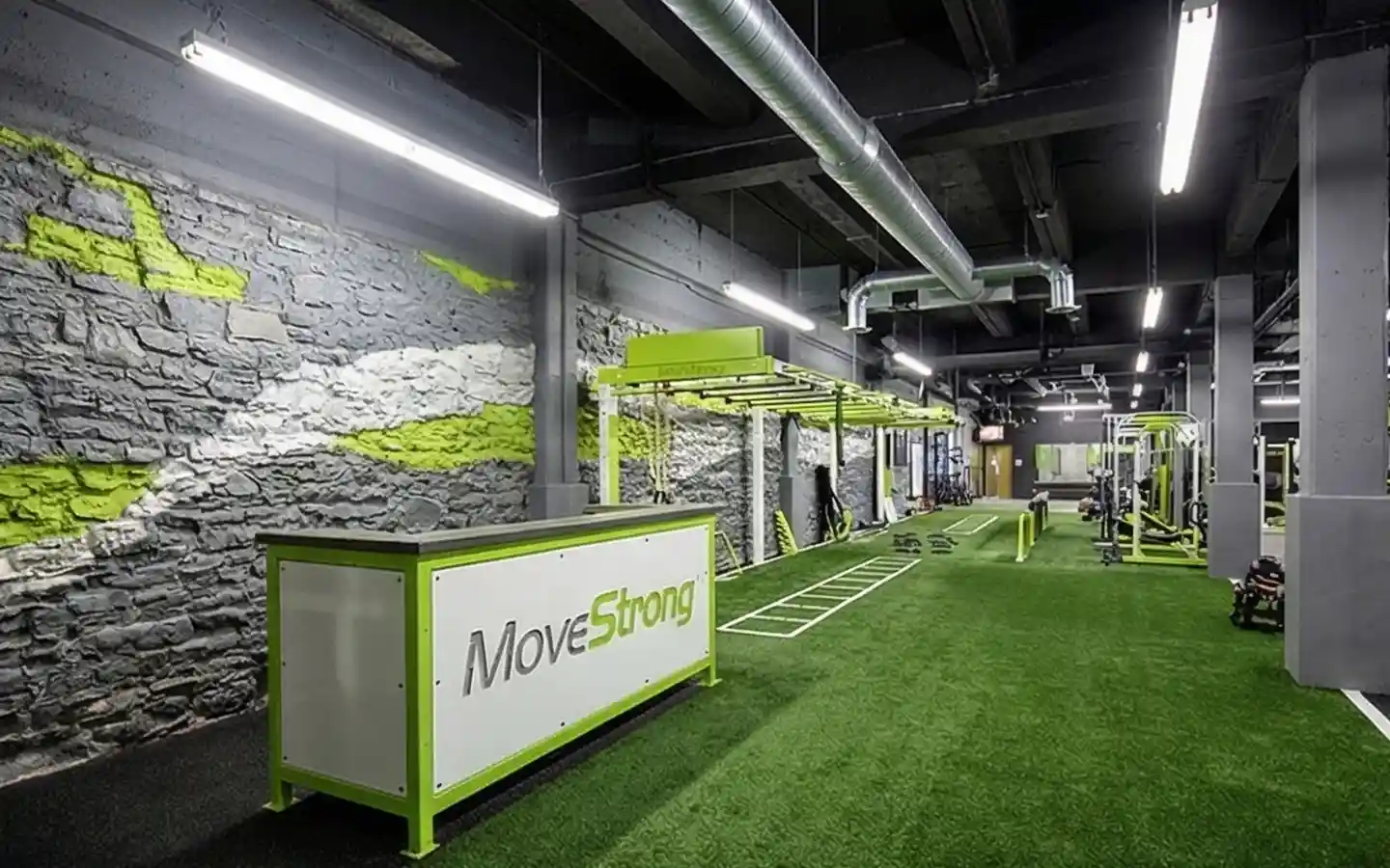Industrial gym interior design featuring green turf flooring, exposed stone walls, and a MoveStrong functional training station