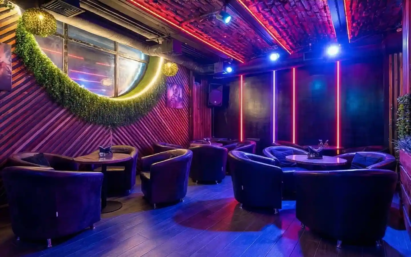 Eclectic pub interior with exposed red brick ceiling, vertical neon light strips, wood-slat walls, and circular greenery accents around a large window