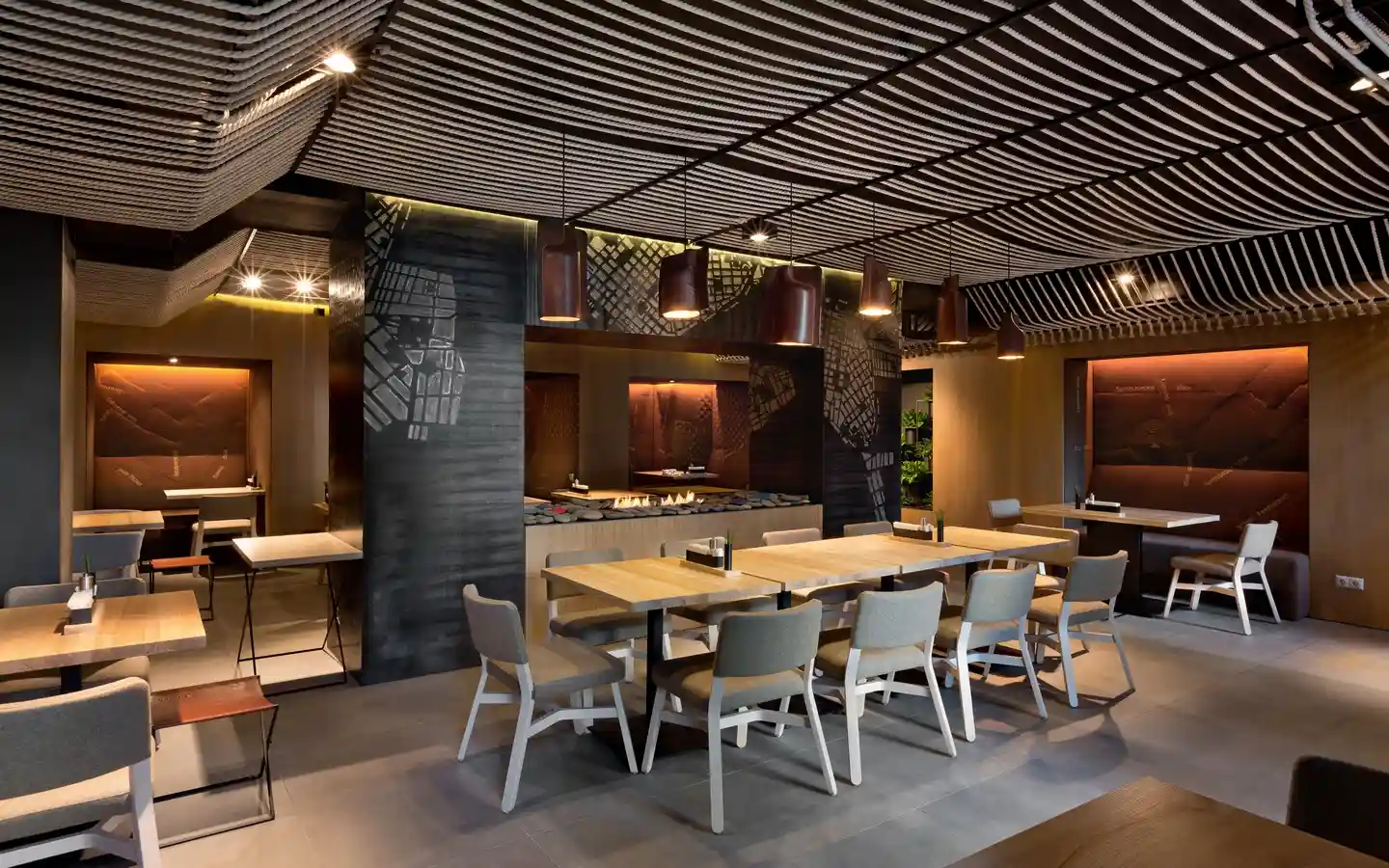 Modern industrial restaurant dining area featuring a decorative rope ceiling, warm pendant lighting, and wooden tables