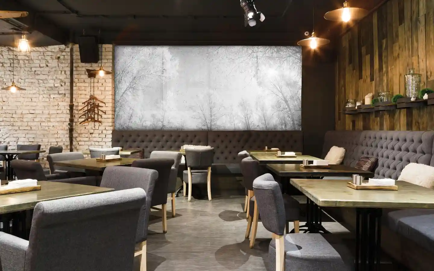 Industrial restaurant interior with tufted banquette seating, exposed brick walls, wood paneling, and large forest mural