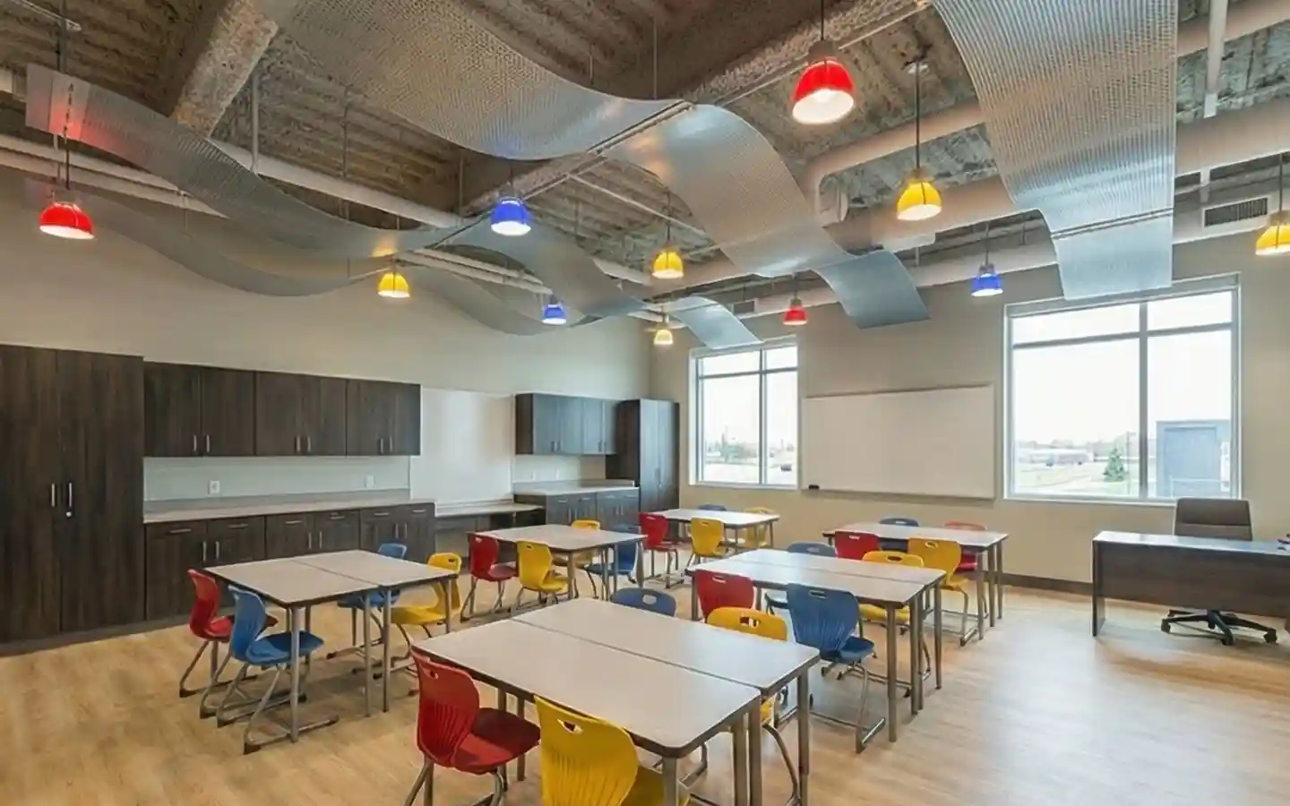 Modern school classroom with wave-style acoustic ceiling panels, colorful pendant lighting, and dark wood cabinetry for student storage