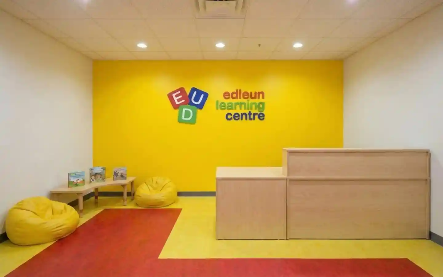 Bright yellow learning centre reception area featuring a wooden front desk, yellow bean bag chairs, and colorful wall branding