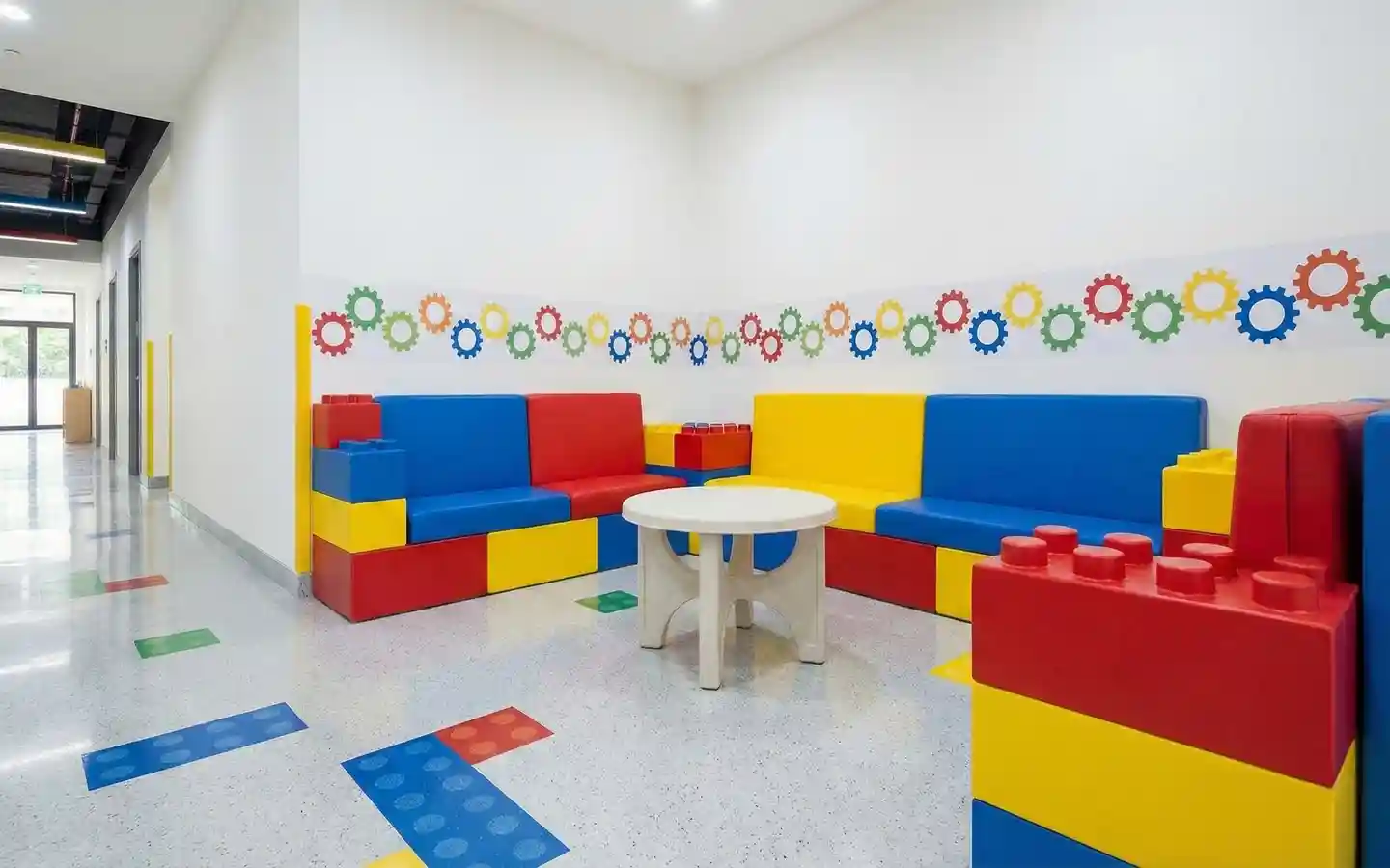 Colorful modular block-themed seating area in a school hallway with primary colored sofas and gear wall decals