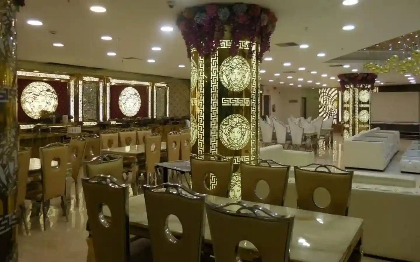 Opulent banquet hall dining area featuring gold-lit decorative pillars, designer Medusa wall art, and high-back upholstered chairs