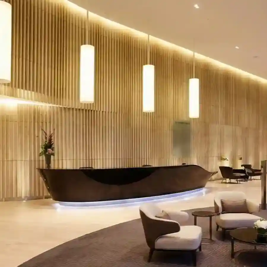 Modern luxury hotel lobby featuring a curved black marble reception desk with wood slat wall paneling and warm pendant lighting