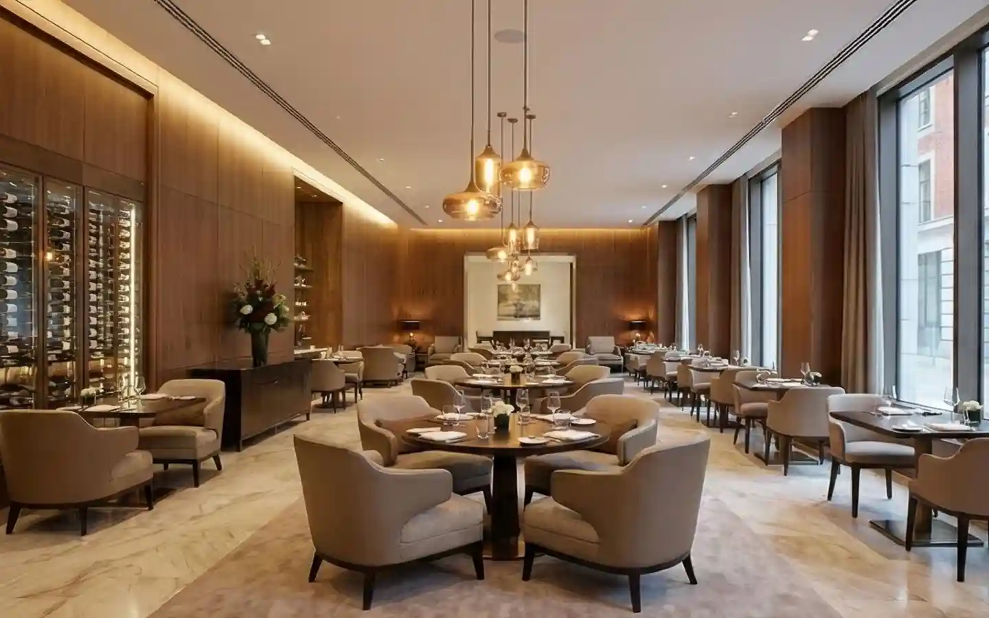 Upscale hotel dining room featuring warm wood wall paneling, circular tables with plush armchairs, and amber glass pendant lighting