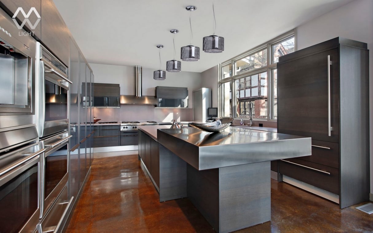 Luxury industrial-style home kitchen featuring a massive stainless steel waterfall island, dark wood cabinetry, polished concrete floors, and designer pendant lighting