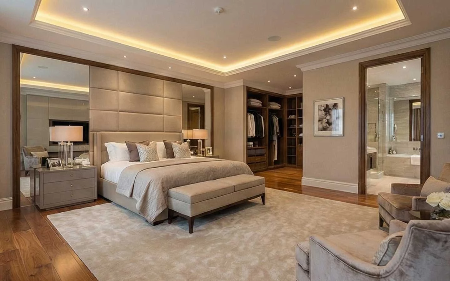 Luxury master bedroom suite featuring a tufted headboard, integrated tray ceiling lighting, an open walk-in closet, and a glimpse of a modern ensuite bathroom