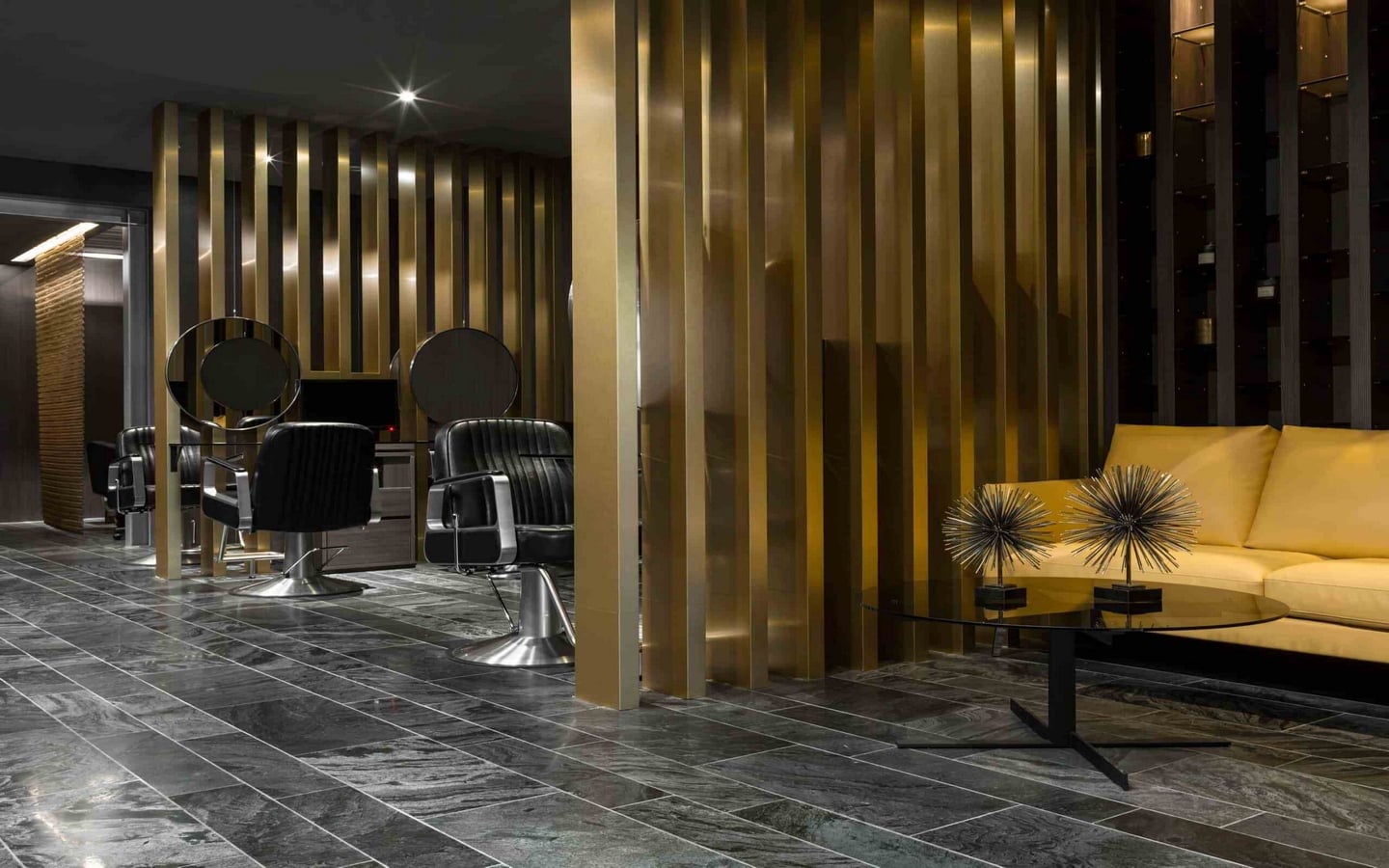 Luxurious modern salon interior with black leather chairs, circular mirrors, gold metallic panels, marble flooring, and stylish lounge area