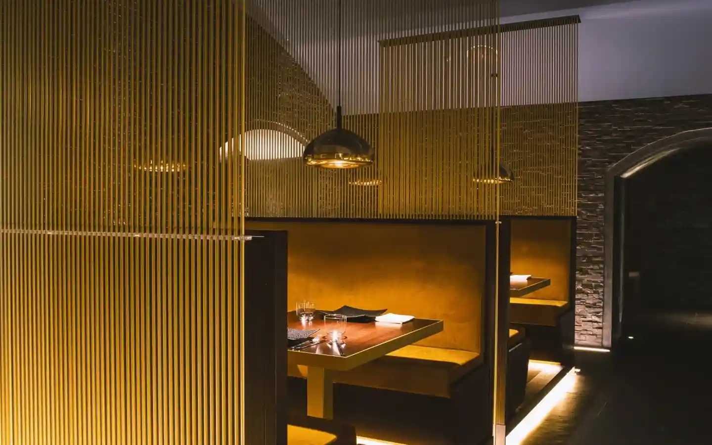 Elegant restaurant booth seating with gold vertical rod partitions, warm ambient lighting, and dark wood tables