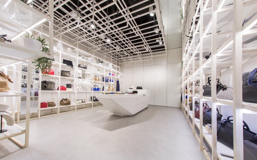 Wide angle view of luxury retail store interior with handbags displayed on illuminated shelving and modern ceiling design