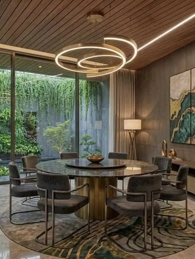 Modern luxury dining room featuring a large round marble table with a built-in lazy susan, velvet dining chairs, and a gold halo chandelier against a vertical garden backdrop
