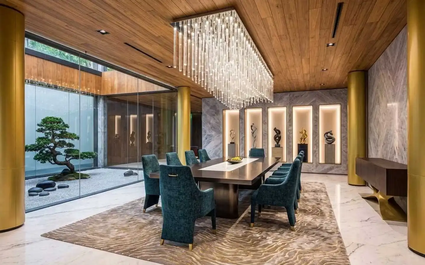 Grand villa dining room featuring a long rectangular crystal chandelier, teal velvet dining chairs, gold architectural pillars, and a glass wall overlooking an indoor Zen bonsai garden