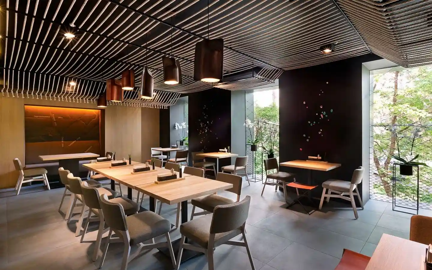Minimalist restaurant interior featuring a unique decorative rope ceiling, modern timber tables, and dark accent walls with large windows
