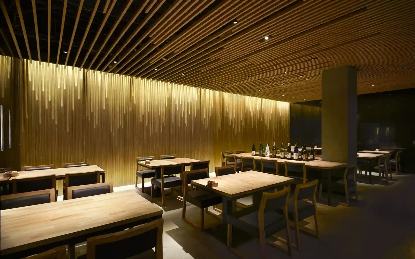 Zen-style restaurant interior featuring a backlit wood slat wall, timber ceiling beams, and minimalist wooden dining furniture
