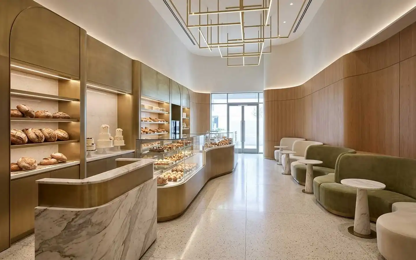 Modern bakery interior featuring curved wood wall panels, marble service counter with gold accents, boutique pastry displays, and sage green velvet seating