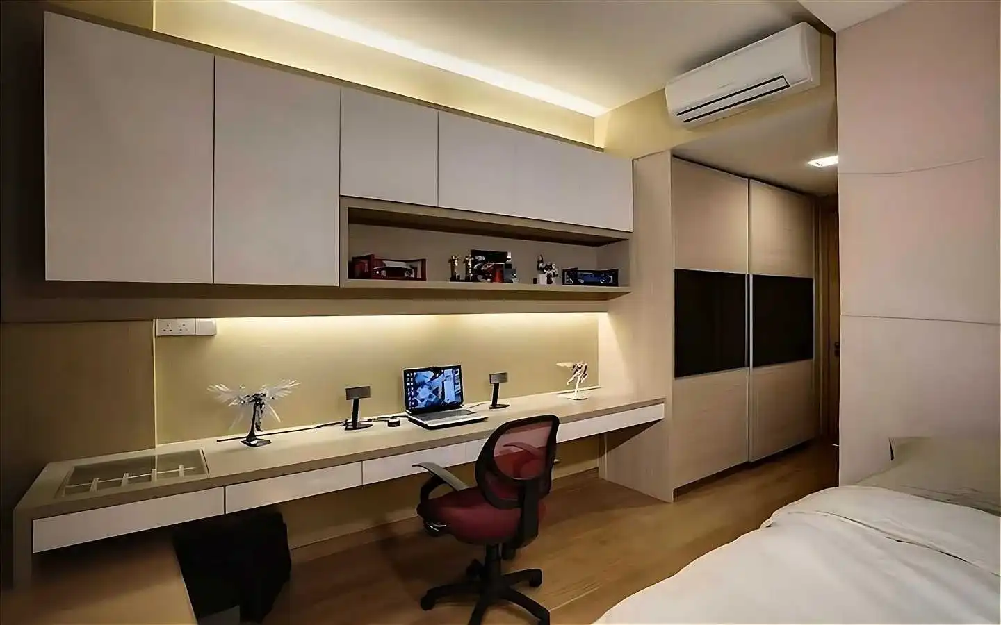 Modern bedroom with a custom built-in study desk, overhead storage cabinets with warm LED profile lighting, a sliding wardrobe, and a ergonomic workstation