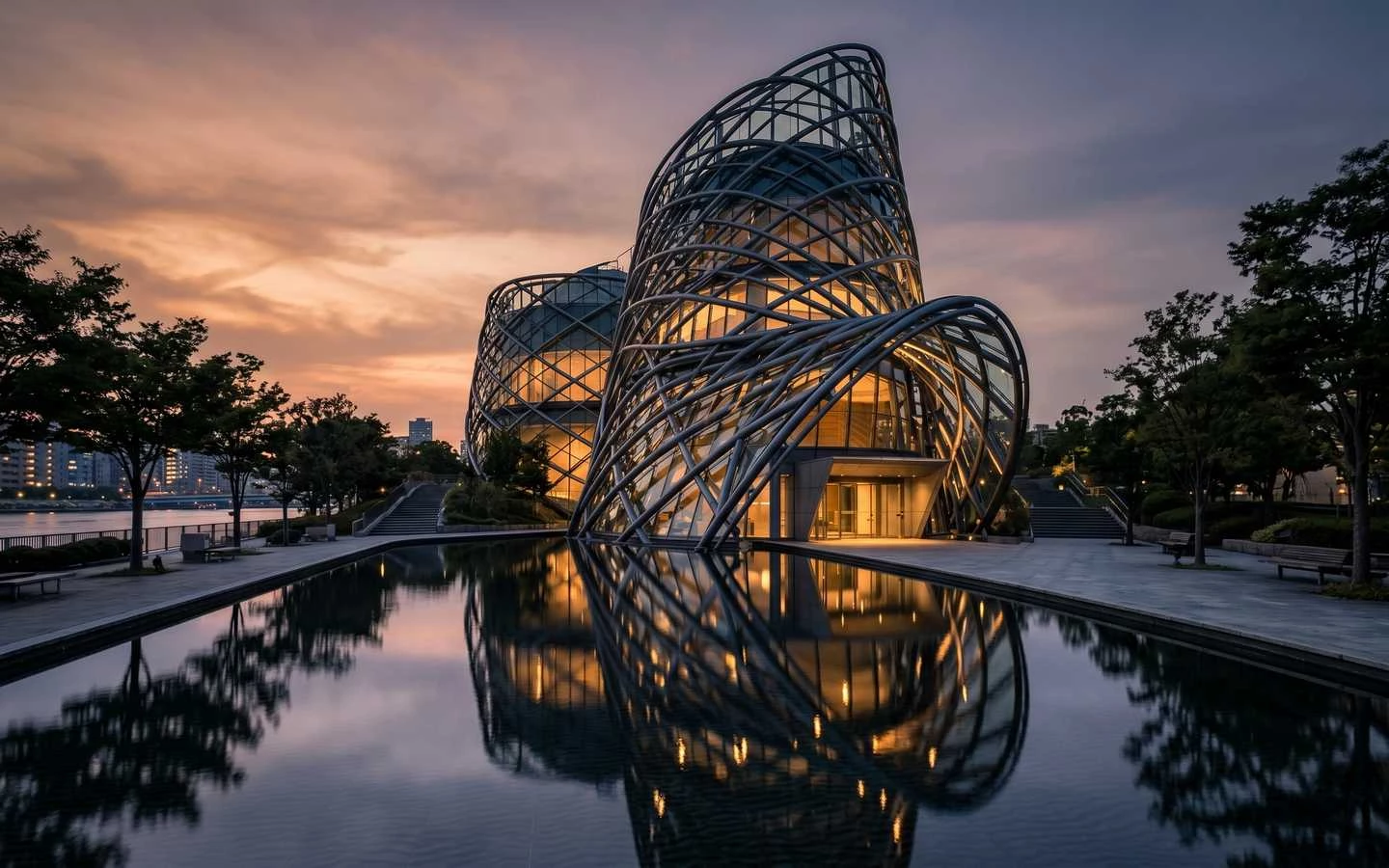 Modern commercial building featuring a woven steel lattice facade and glass exterior reflected in a plaza pool at sunset