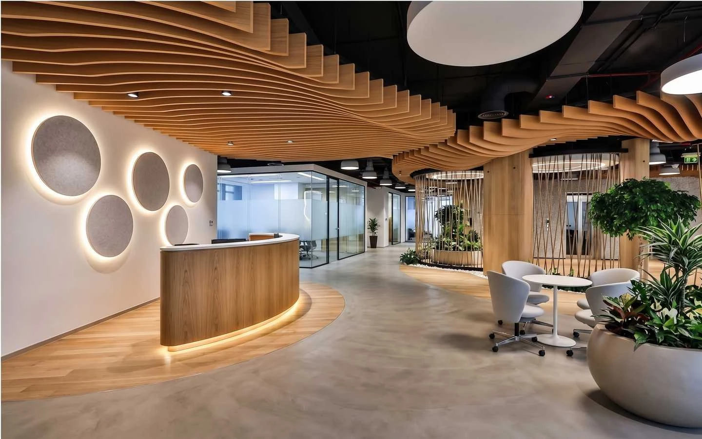 Modern biophilic office reception area featuring a curved wooden desk, wave-patterned ceiling baffles, and indoor greenery