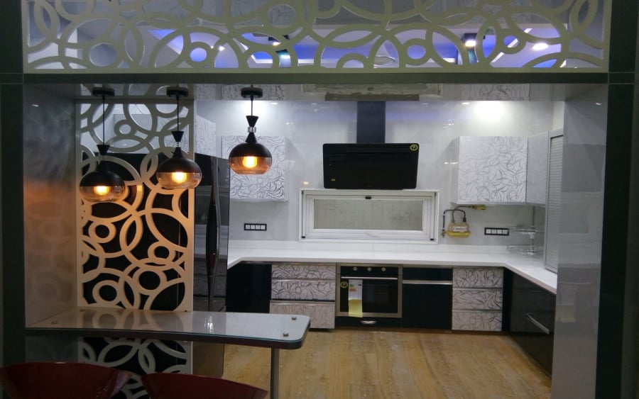 Modern open kitchen interior featuring black and patterned white cabinets, a white circular cutout partition wall, and a small breakfast counter illuminated by three hanging pendant lights