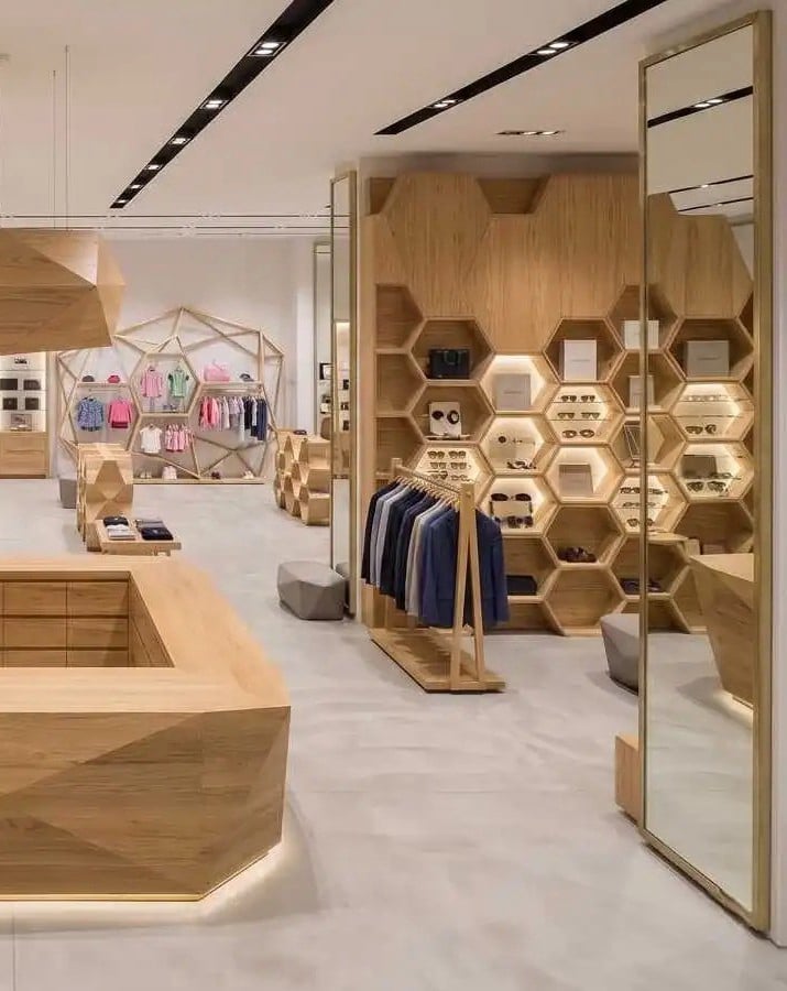 Modern boutique showroom interior featuring unique honeycomb-shaped wood wall shelving, geometric display counters, and minimalist clothing racks