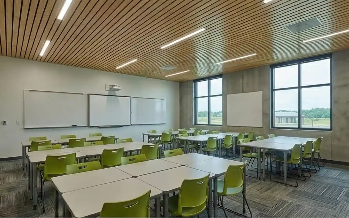 Modern school classroom featuring lime green ergonomic chairs, modular group desks, and a wood-slat acoustic ceiling design