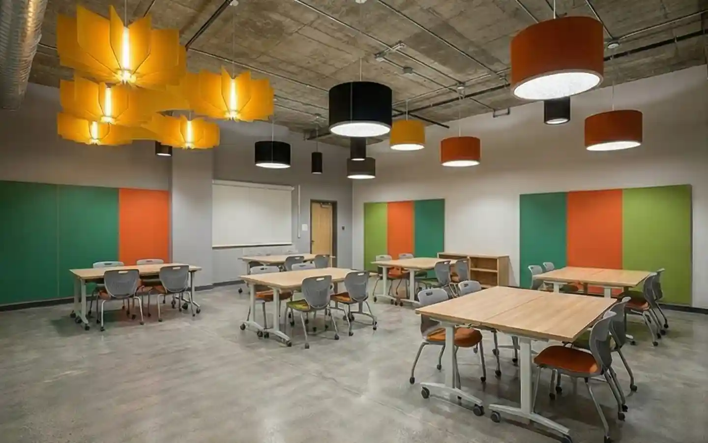 Industrial style school classroom interior with exposed concrete ceilings, colorful acoustic wall panels, and large modern pendant lighting
