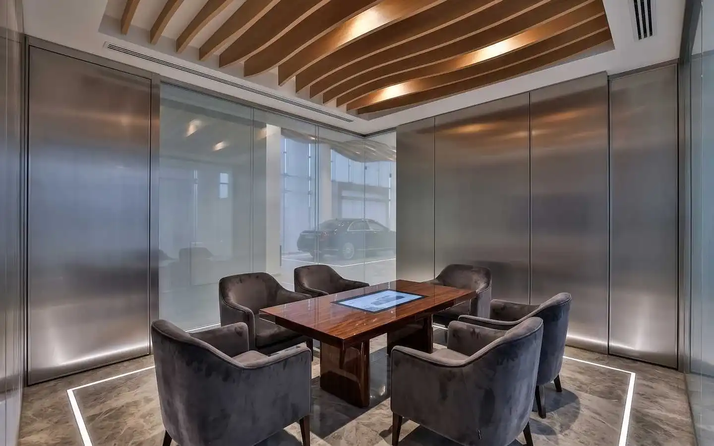Modern commercial meeting room featuring brushed metal wall panels, a wood slat wave ceiling, and a luxury conference table with velvet armchairs