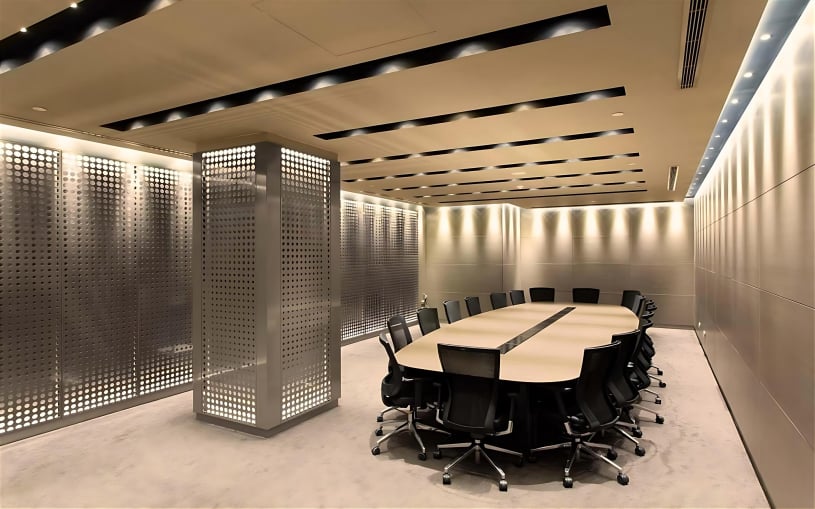Modern corporate boardroom featuring a large oval conference table, ergonomic black chairs, and architectural perforated metal wall panels with integrated LED backlighting