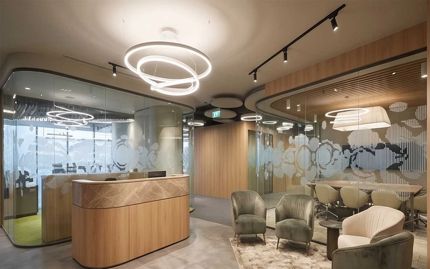 Modern corporate office interior featuring a marble-top reception desk, curved glass partitions with privacy decals, circular pendant lighting, and a view into a professional conference room