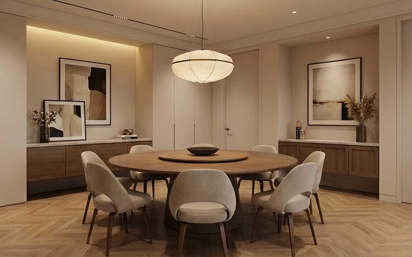 Modern dining room featuring a large round wooden dining table with a lazy susan, beige upholstered chairs, a pendant paper lantern light, and chevron wood floors