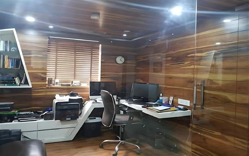 Modern home office featuring rich wood-paneled walls and ceiling, a custom white corner desk with integrated shelving, and dual monitor setup with ergonomic chair