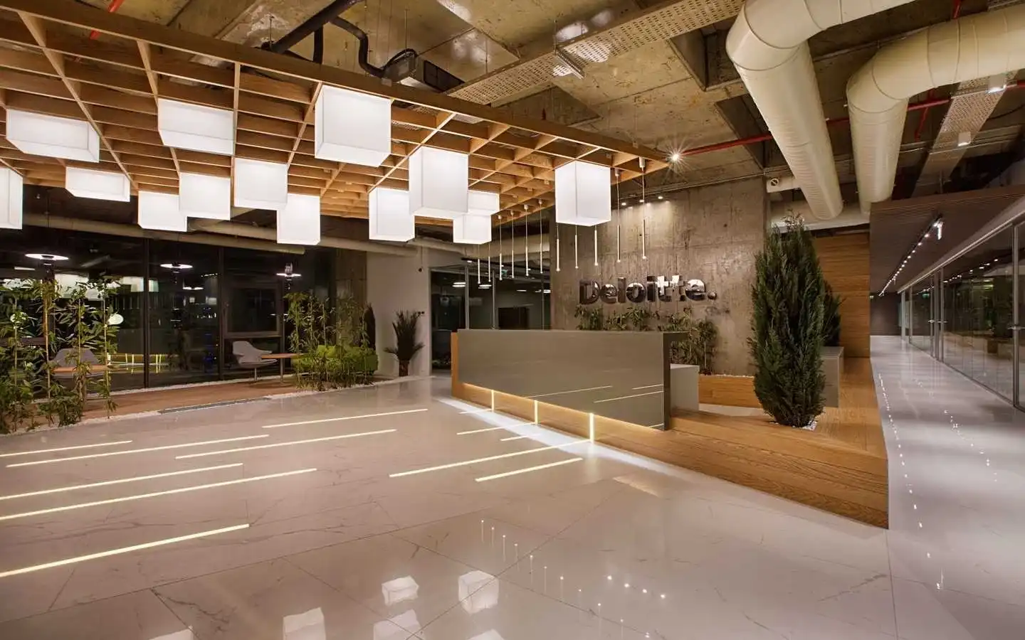 Modern industrial corporate office reception interior design featuring a sleek illuminated front desk, an exposed concrete ceiling with visible ductwork, a custom wooden grid with cube pendant lights, and glossy tile flooring