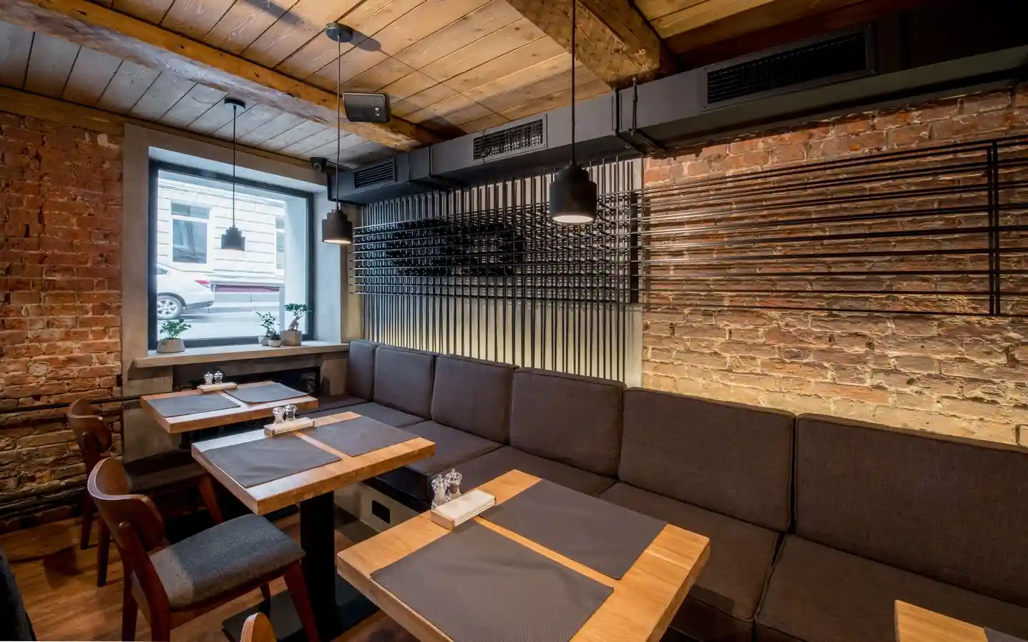 Modern industrial restaurant interior featuring exposed brick walls, wooden ceilings, and dark grey banquet seating