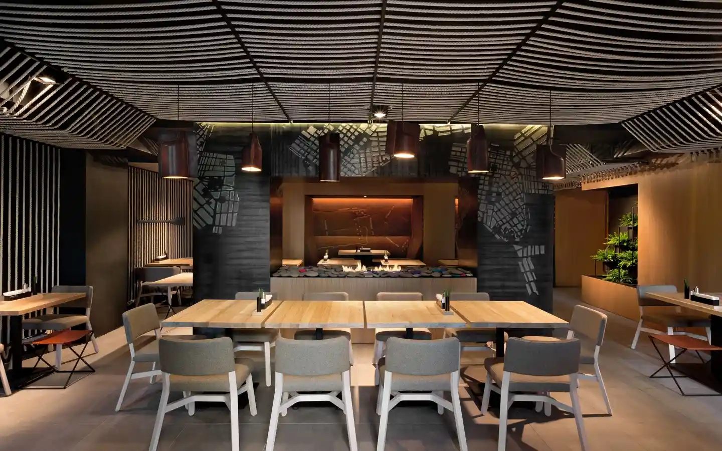 Modern industrial restaurant interior featuring a unique decorative rope ceiling, dark accent walls with mural art, and light wood dining tables with grey upholstered chairs