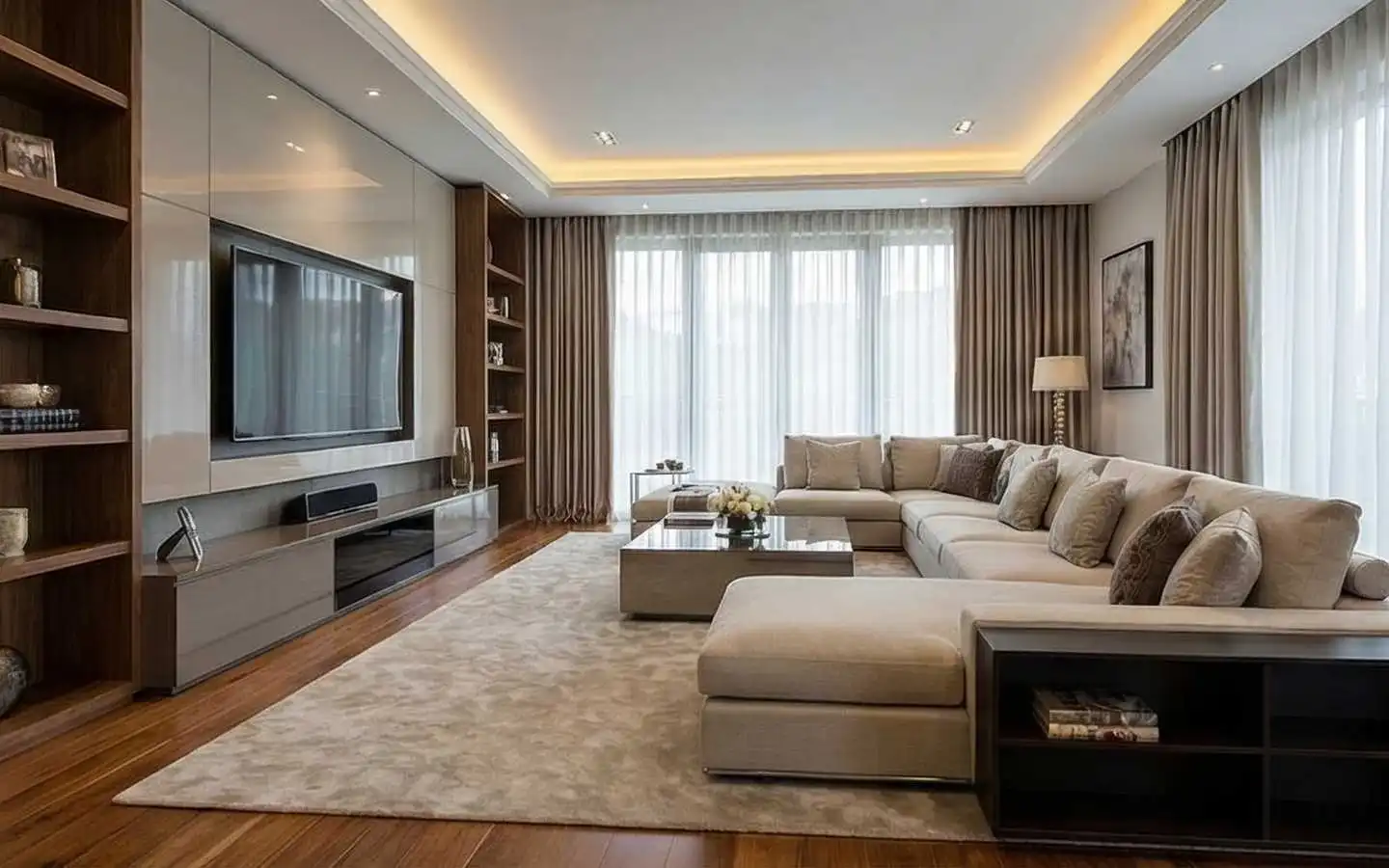Modern living room design featuring a custom built-in entertainment unit, a large beige l-shaped sectional sofa, floor-to-ceiling curtains, and warm recessed ceiling lighting